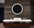 Bathroom vanity with a round illuminated mirror on a wooden wall.