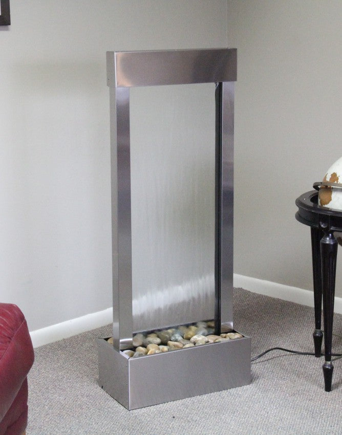 Silver indoor water fountain with pebbles on a gray carpeted floor.