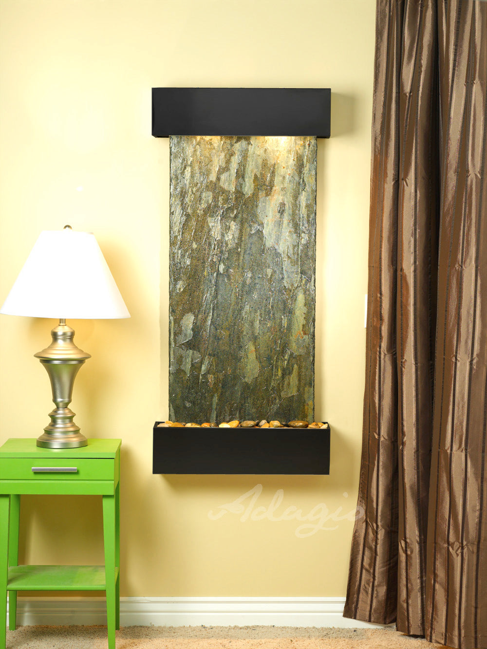 Wall-mounted water feature green slate with a lamp and green side table against a yellow wall.