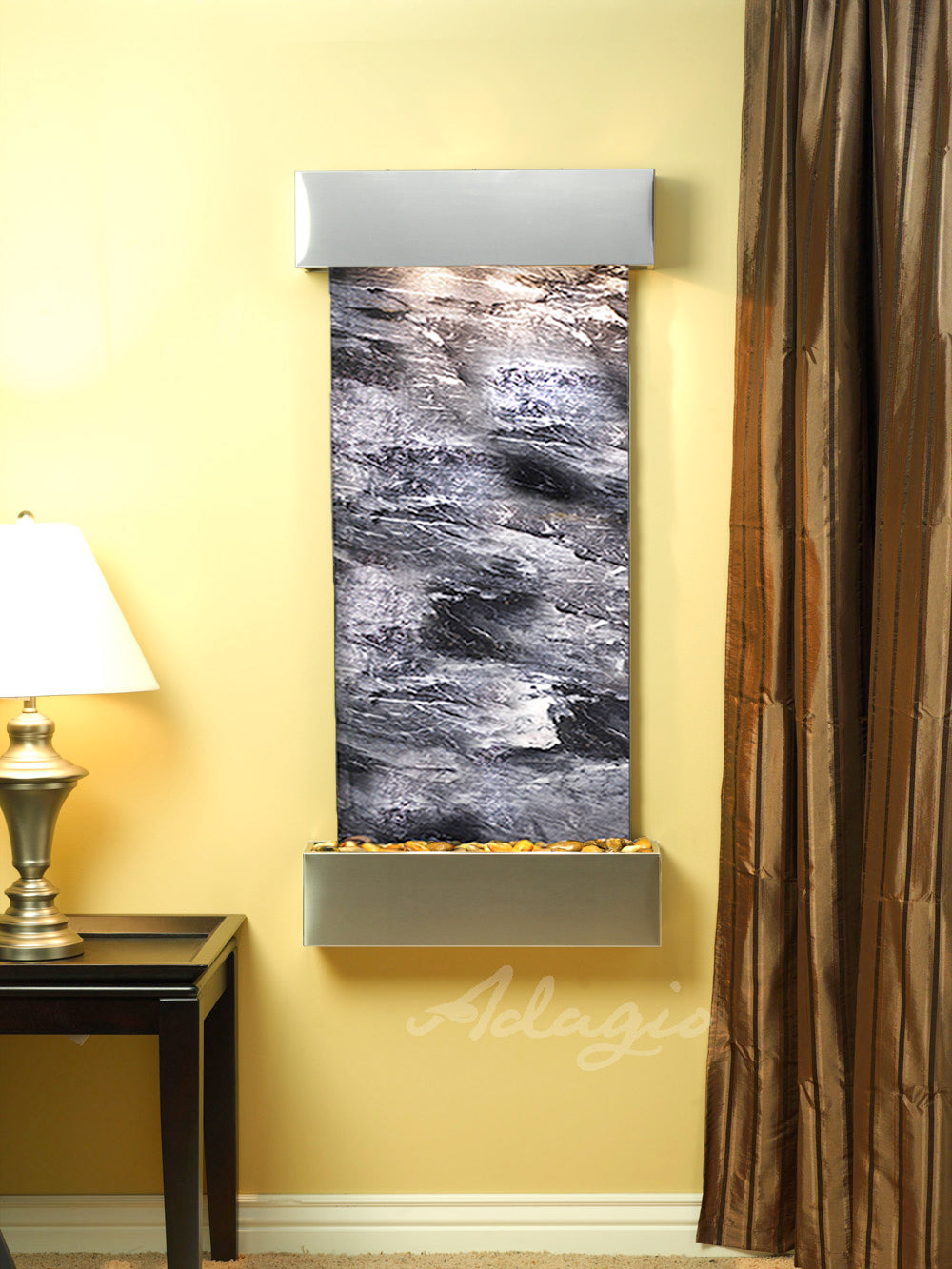 Decorative wall fountain with black spider marble on a yellow wall, next to a lamp and brown curtain.