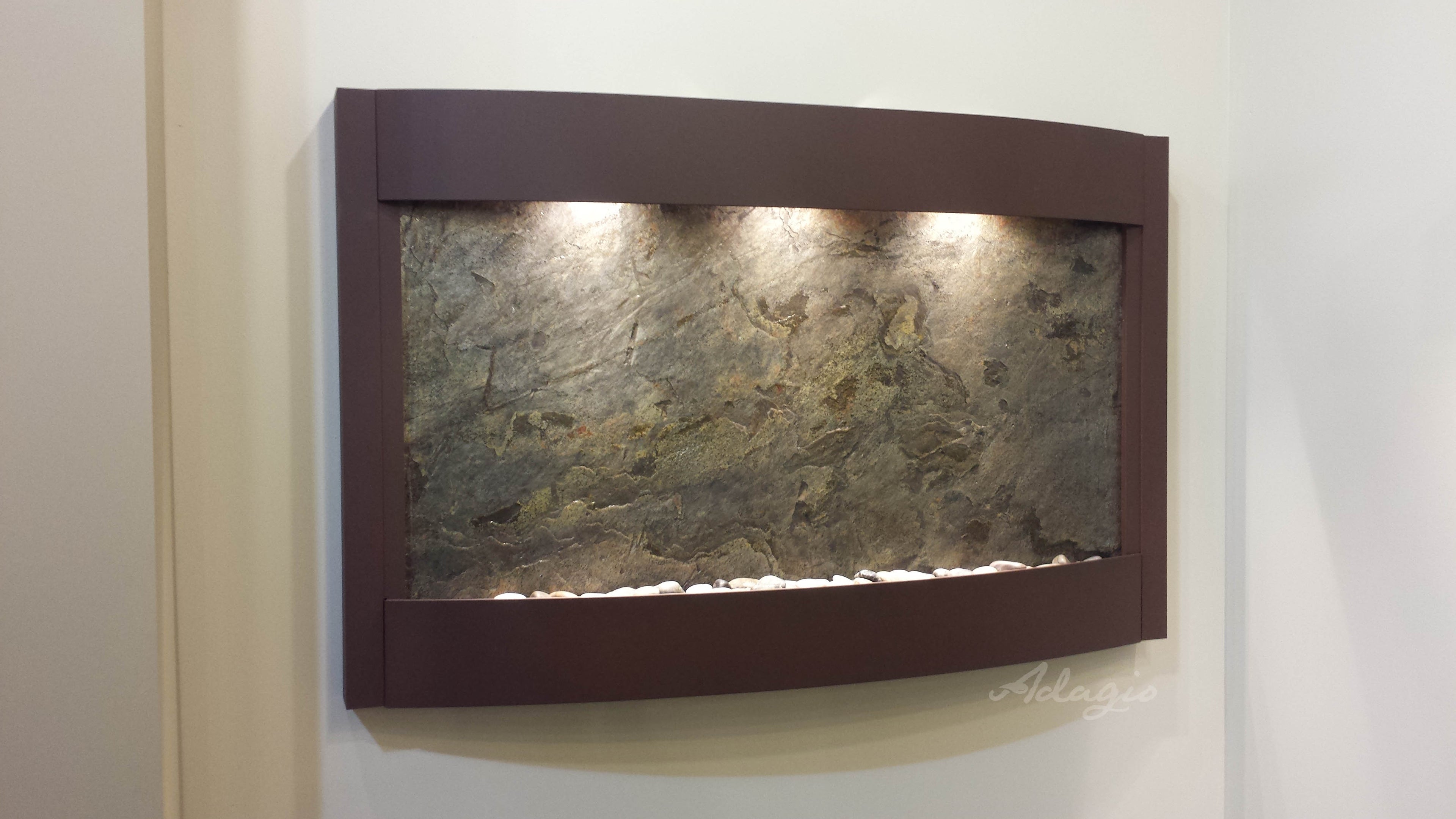 Wall-mounted fountain with stone-like texture and brown frame on a white wall.