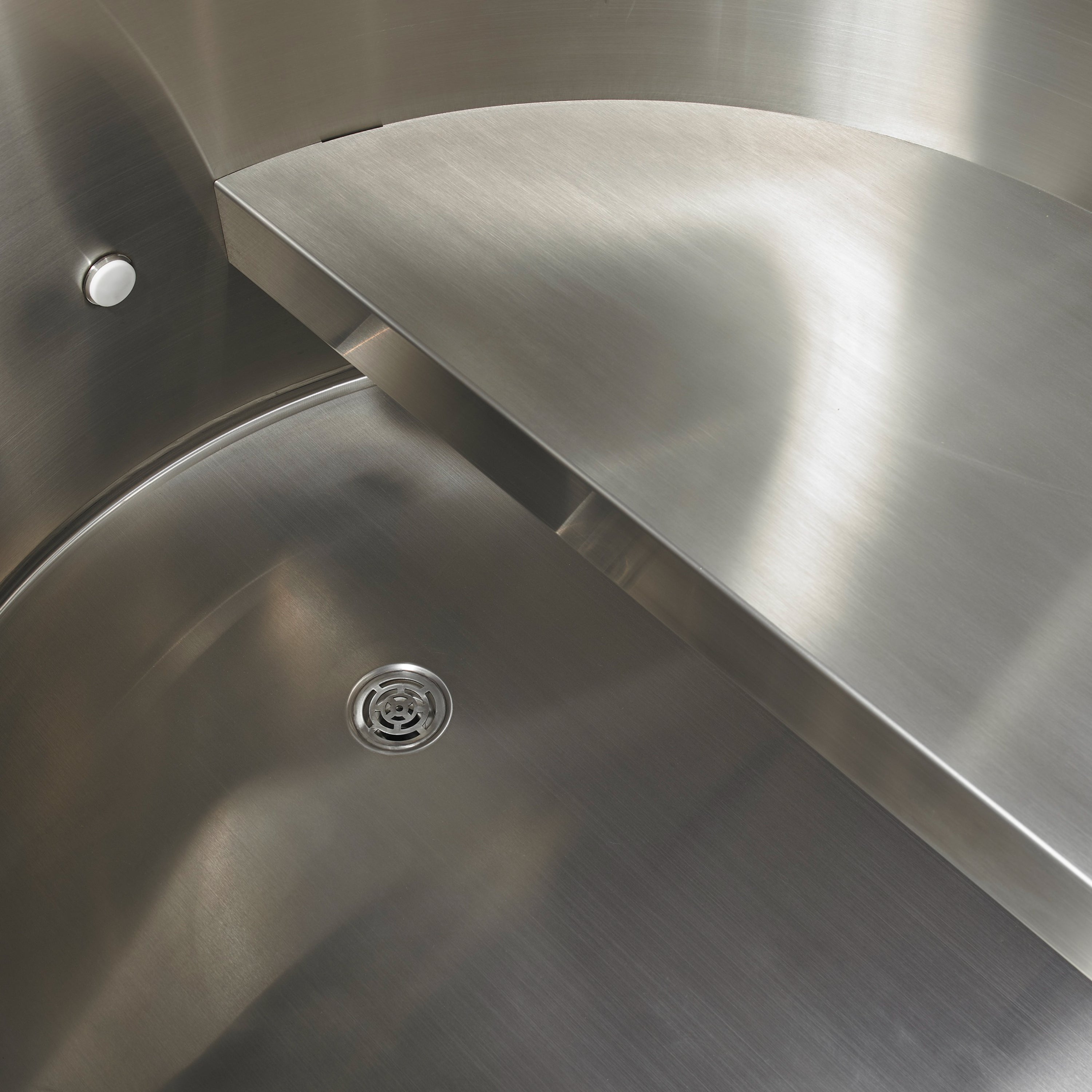 Close-up of a stainless steel tub with a drain and bench.