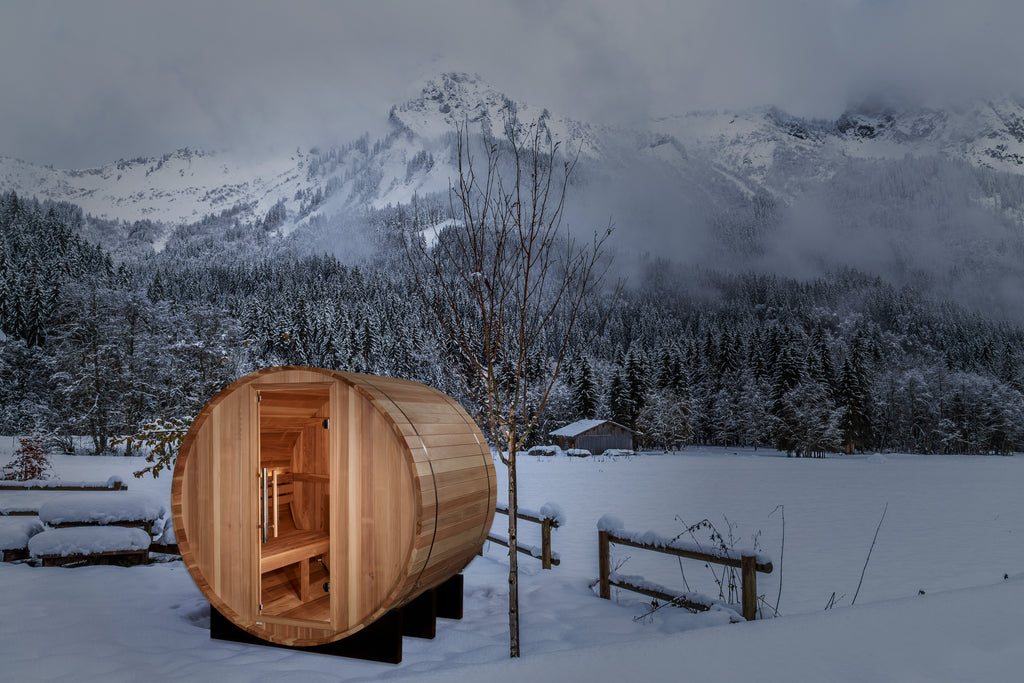 Wooden barrel sauna in a snowy landscape with mountains in the background