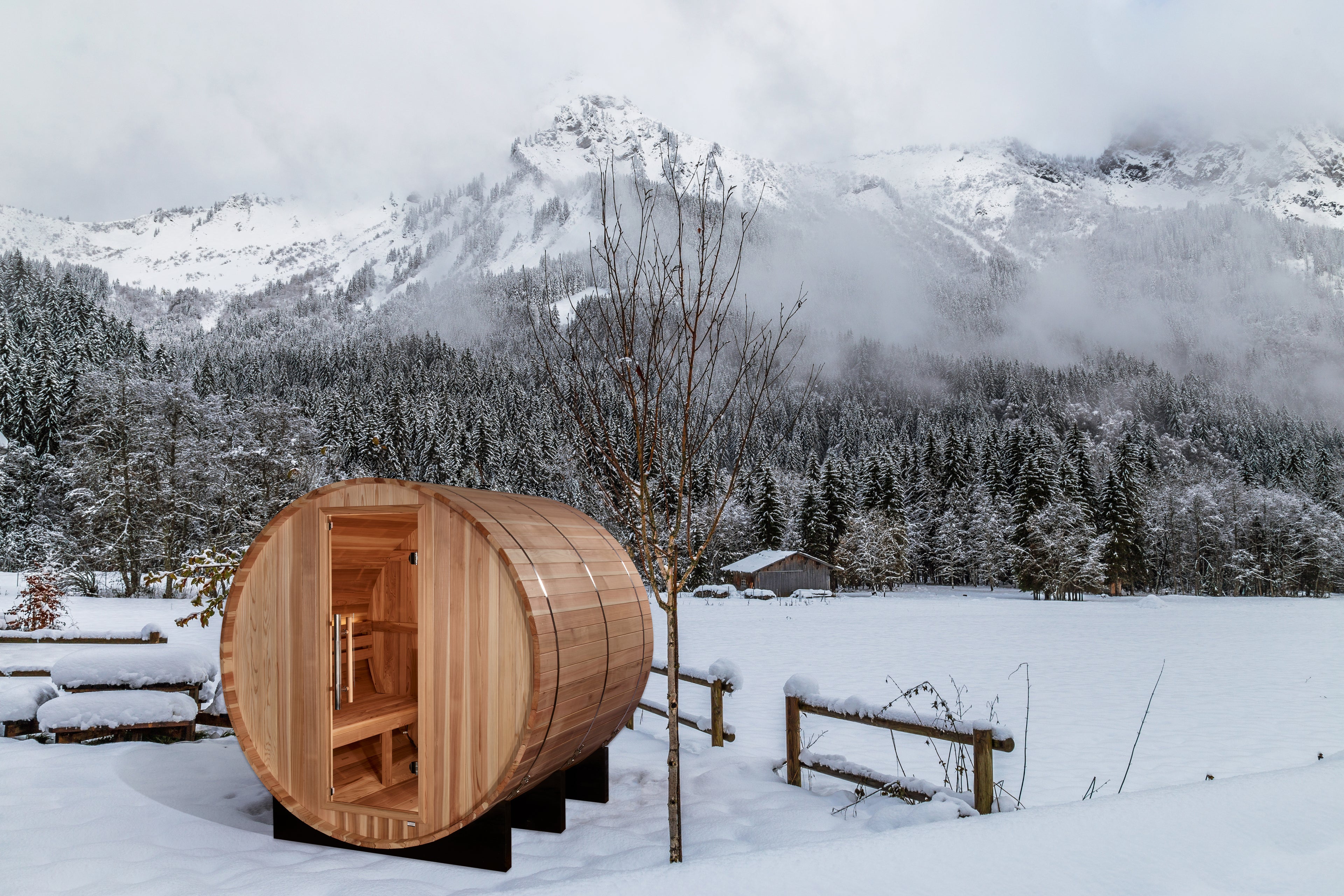 Wooden barrel-shaped sauna in a snowy landscape with mountains in the background