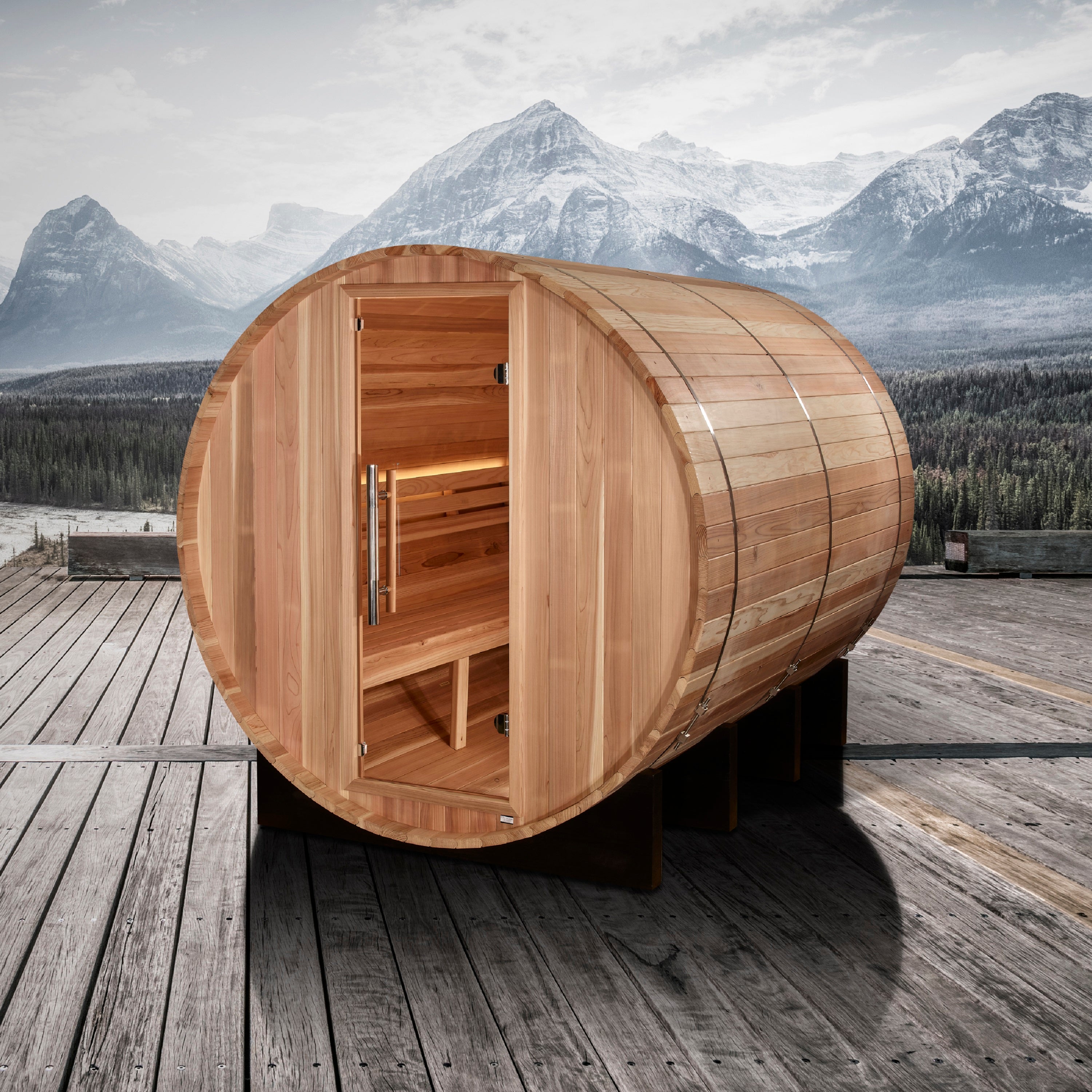 Wooden barrel-shaped sauna on a wooden deck with mountains in the background