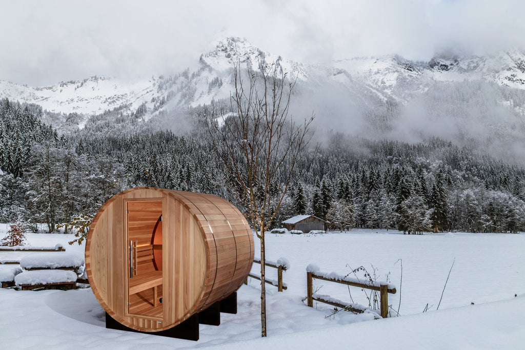 Wooden barrel sauna in a snowy landscape with mountains in the background