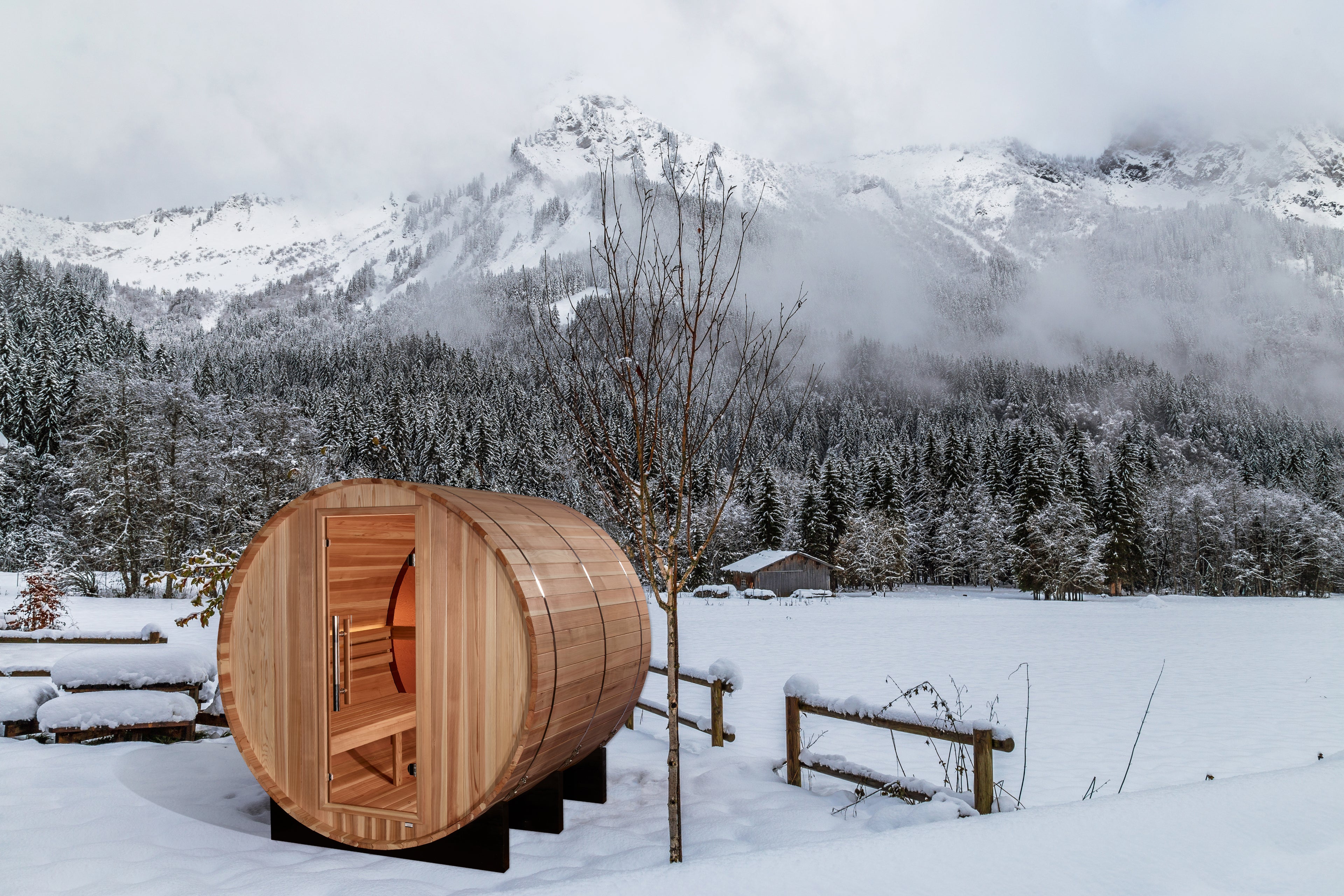 Wooden barrel sauna in a snowy landscape with mountains in the background
