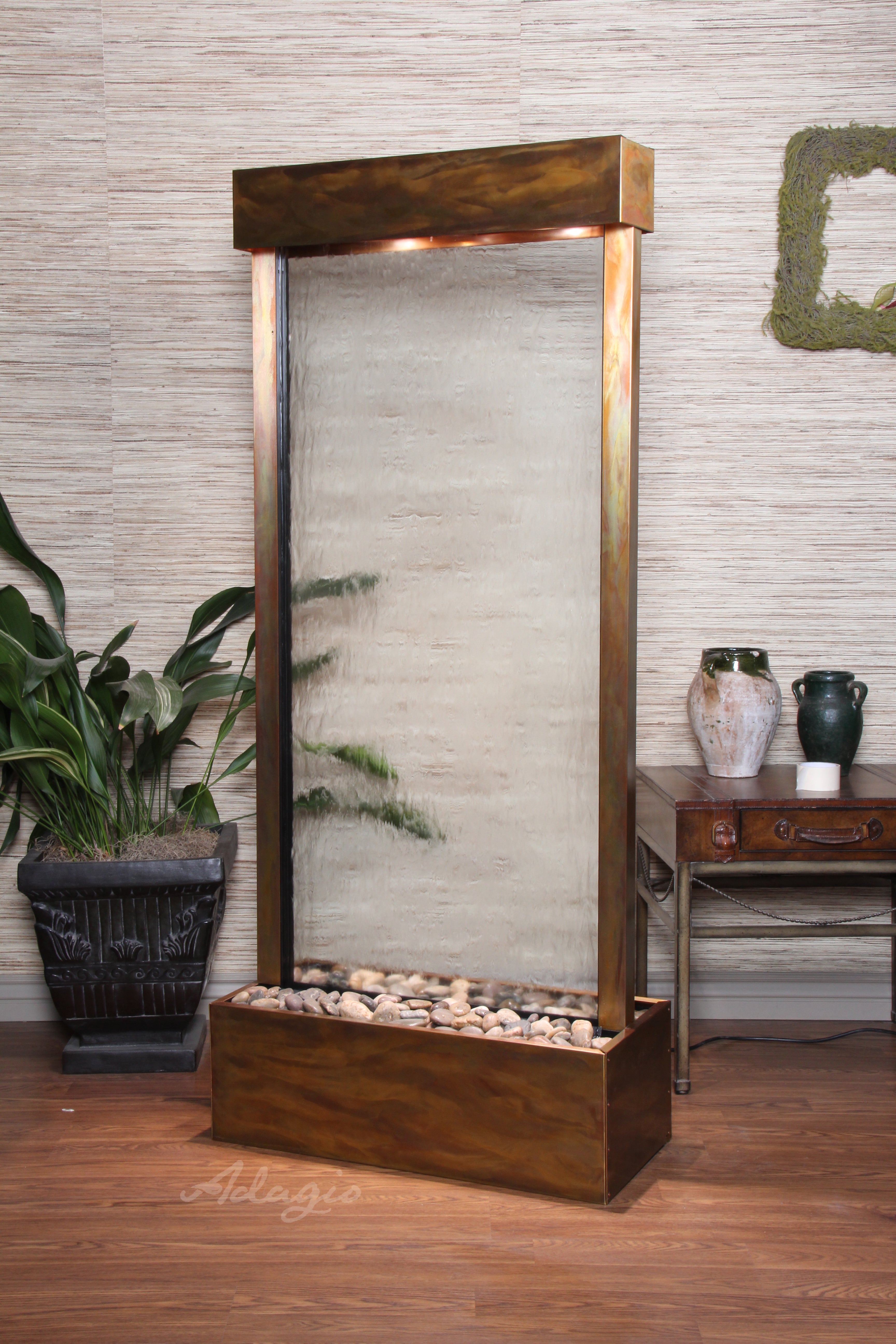 Wooden indoor fountain with rocks and light fixture against a textured wall.