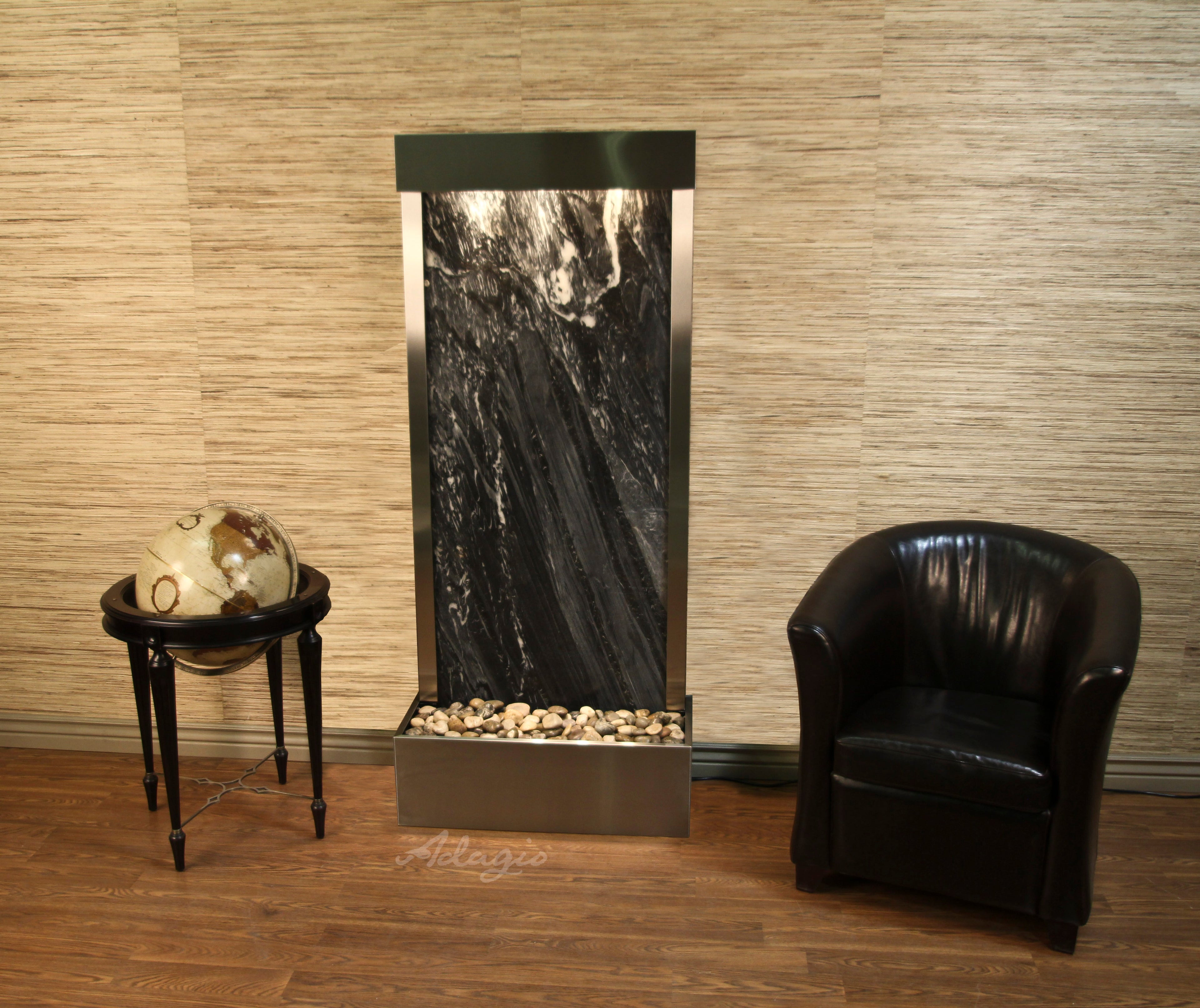 Fountain with decorative stones in a room with a black chair and small table.