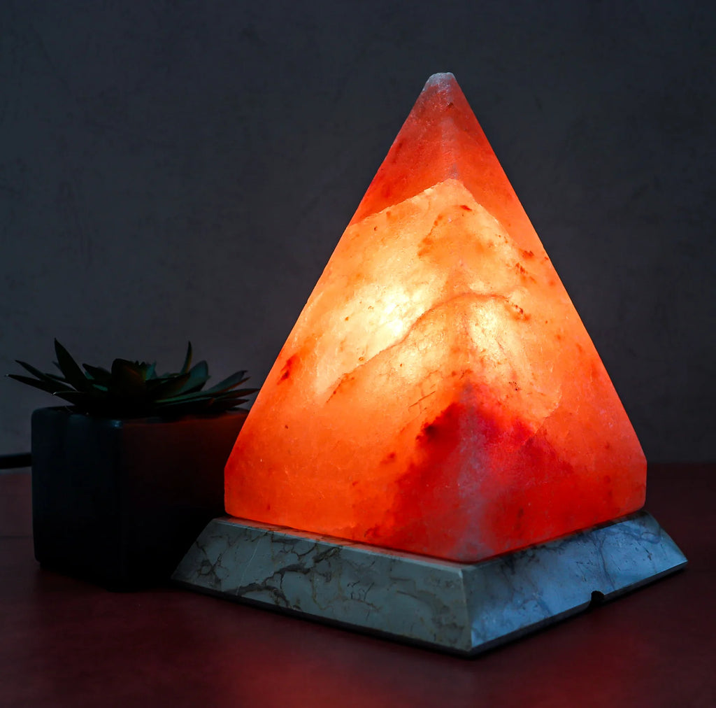 Triangular Himalayan salt lamp on a dark background with a small plant.