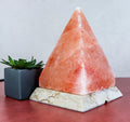 Pyramid-shaped pink salt lamp on a marble base with a small plant in the background.