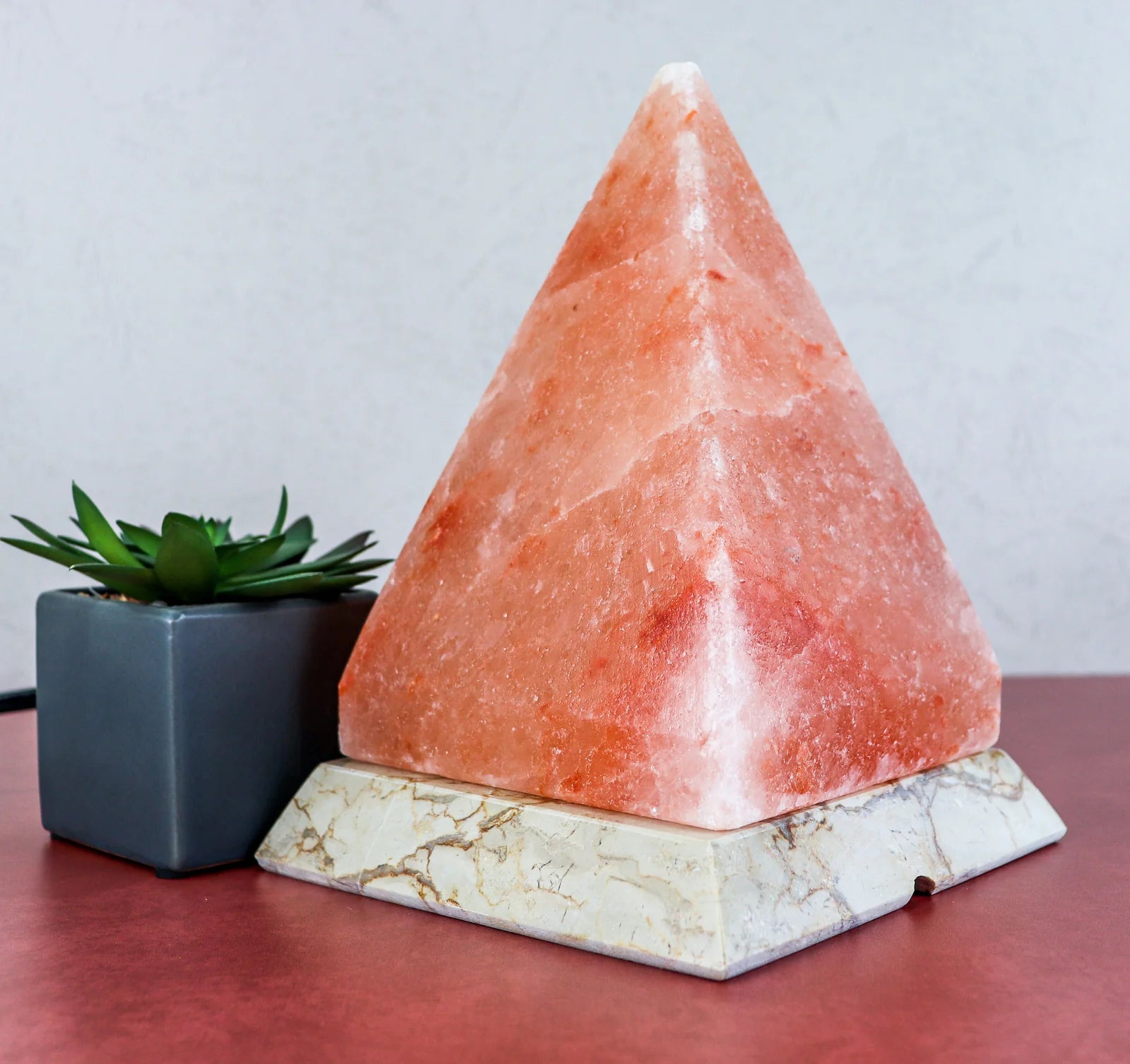Pyramid-shaped pink salt lamp on a marble base with a small plant in the background.