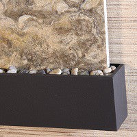 Black rectangular trim with pebbles against a stone wall